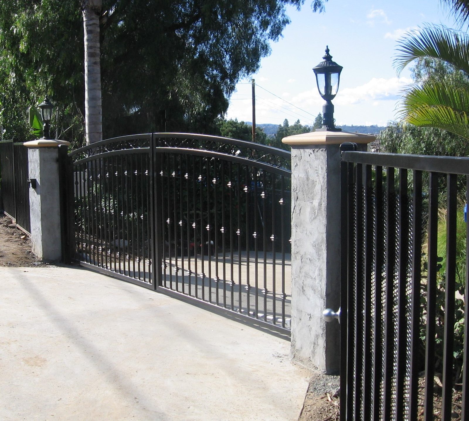 Arched ornamental iron driveway gate with stucco pillars built by HD Fence